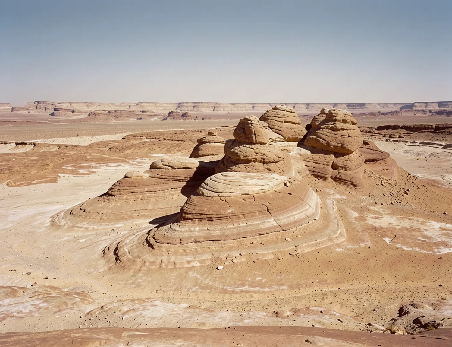 Layered sunbaked sandstone with a distant horizon beneath a clear daylight sky