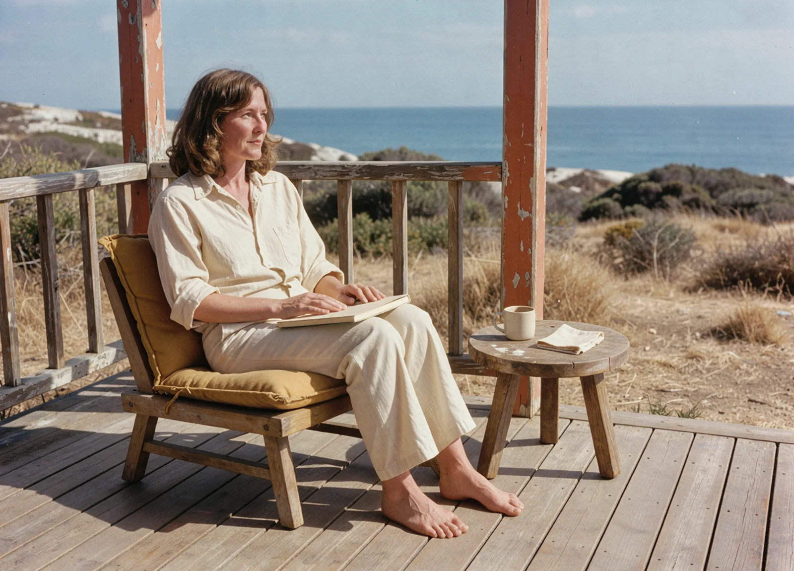 An adult sitting on a sunny porch with a plain closed notebook and a mug